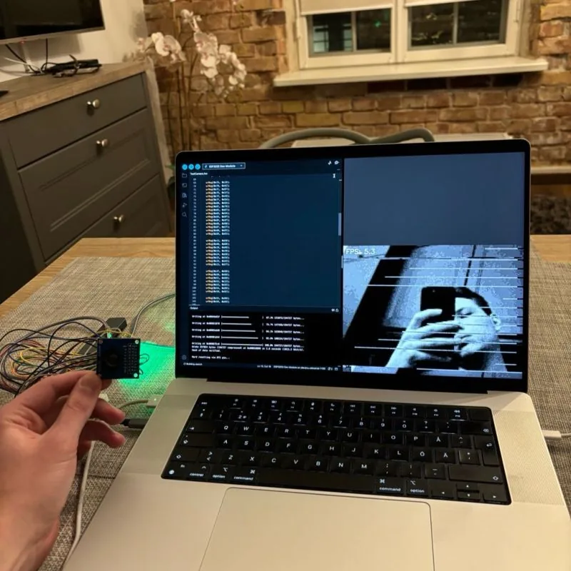 ESP32-S3 wired to a tiny OV7670 module on the left; a live 5.3 FPS grayscale capture from the camera on the right of the laptop screen